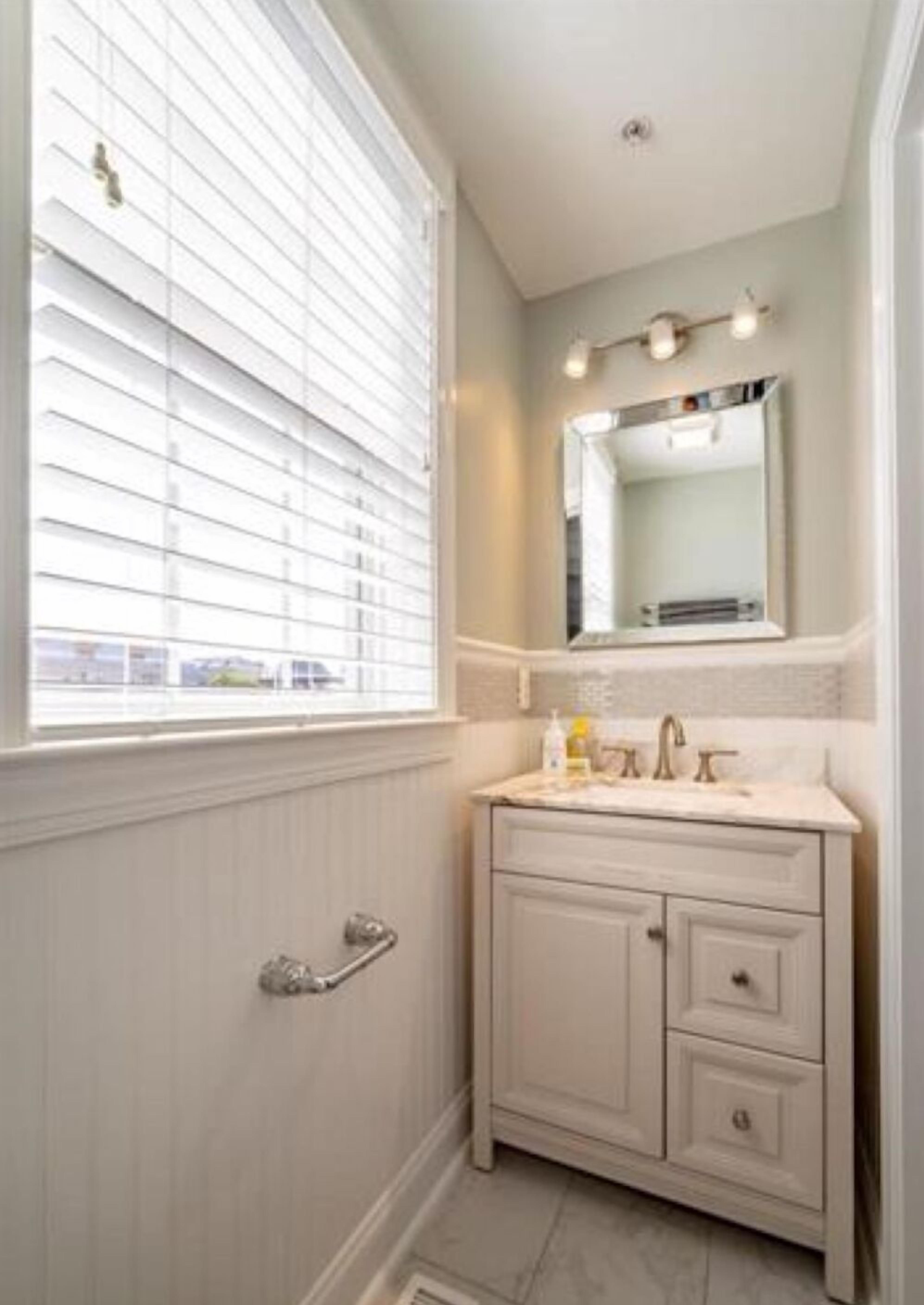 Une salle de bain avec un meuble-lavabo, un miroir et une fenêtre équipée de stores.
