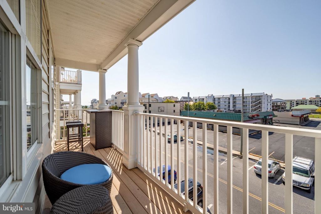Ein Balkon mit Korbmöbeln, Blick auf einen Parkplatz und Gebäude im Hintergrund.