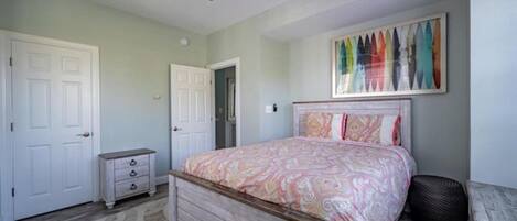 A bedroom with a bed, a ceiling fan, a door, a dresser, and a colorful artwork on the wall.