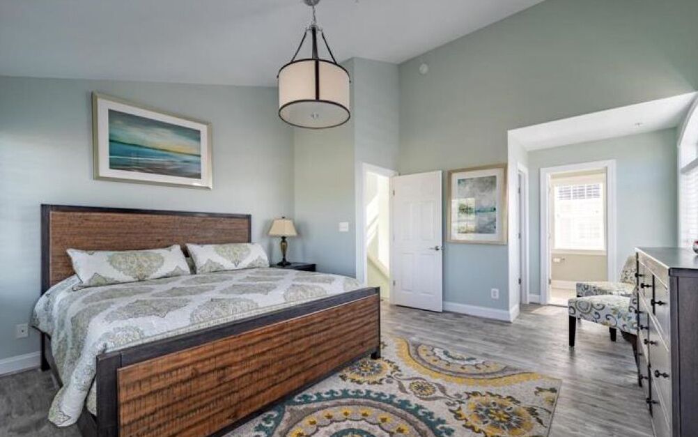 A bedroom with a wooden bed, a nightstand, a lamp, and a patterned rug.