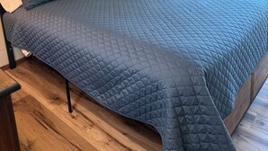 Un dormitorio con una cama grande, piso de madera y dos cuadros en la pared.