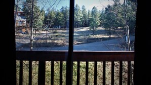 Vista a través de una ventana de madera que muestra un área cubierta de césped con árboles y una carretera.