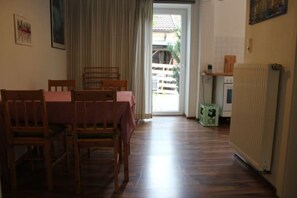 A dining area with a table and chairs, a radiator, and a view through a door to the outside.