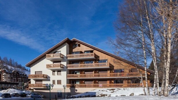 A multi-story hotel with wooden balconies and a ski slope in the background.