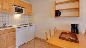 A compact kitchen with wooden cabinets, a microwave, a dishwasher, a coffee maker, and a wooden dining table with chairs.