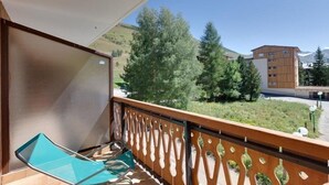 A balcony with a view of a mountain and trees, a wooden railing, and a blue chair.