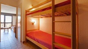 A bunk bed with a red mattress in a room with hexagonal tile flooring and a window.