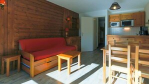 A cozy living area with a wooden sofa, a small wooden table, and a kitchen with wooden cabinets and a microwave.