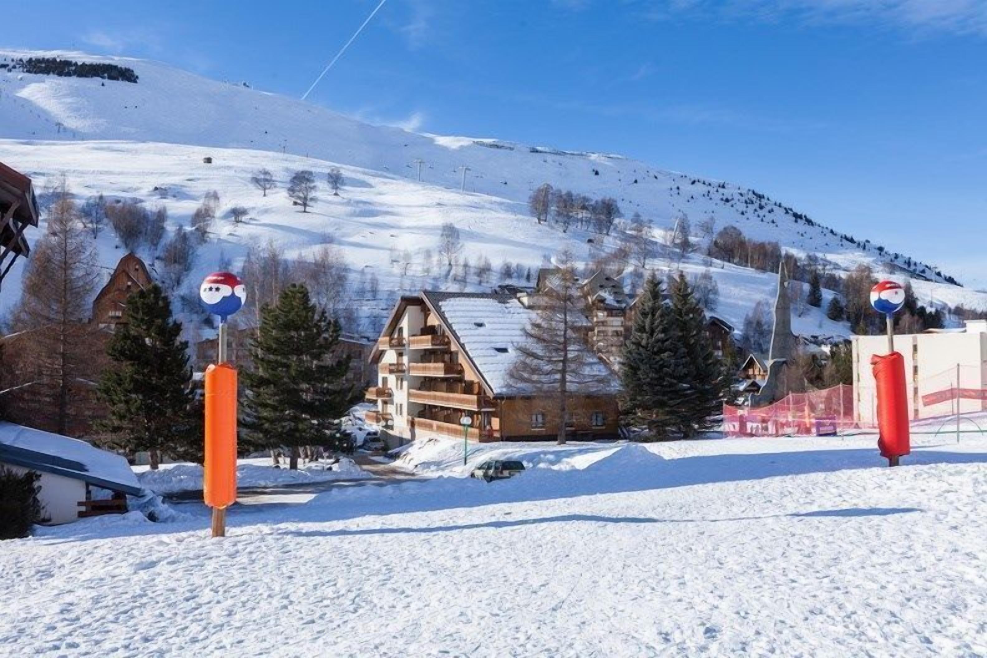 A snow-covered landscape with a wooden chalet and a ski lift in the background.
