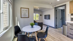 A modern kitchen with a built-in dishwasher, a dining area with a round table and chairs, and a living area with a sofa and a TV mounted on the wall. - ► Modern Tiny House ◄ Big Personality, AC & Views! (Tukwila)