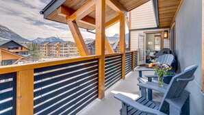 A balcony with wooden railings and a table with chairs, overlooking a mountainous landscape. - Spectacular 3 bedroom Penthouse - Vaulted! Views! (Canmore)