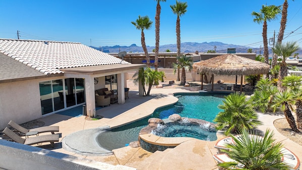 A resort with a swimming pool, lounge chairs, and palm trees.