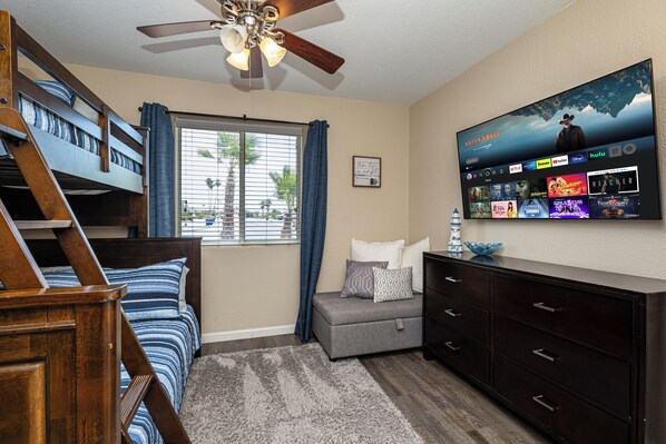 A bedroom with a bunk bed, a desk, a dresser, a TV mounted on the wall displaying various streaming services, and a window with curtains. - River Oasis (Lake Havasu City)