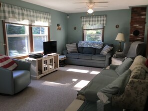 A living room with a grey sofa, a television on a cabinet, and a ceiling fan. - Country Haven (Whitefield)