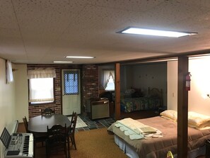 A compact room with a dining table, chairs, a bed with a quilt, a small kitchenette, and a window with curtains. - Country Haven (Whitefield)