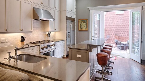 A kitchen with white cabinets, a stainless steel range hood, a sink, and a bar area with stools. - Liberty Street Redbrick Town & Carriage House,  Sleeps 8, Private Parking (Savannah)