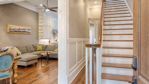 A living room with a wooden staircase, a sofa, a coffee table, and a ceiling fan. - Liberty Street Redbrick Town & Carriage House,  Sleeps 8, Private Parking (Savannah)