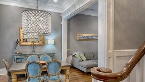 A dining area with a wooden table and chairs, a chandelier, a painting on the wall, and a staircase. - Liberty Street Redbrick Town & Carriage House,  Sleeps 8, Private Parking (Savannah)