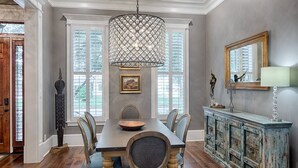 A dining room with a wooden table, six chairs, a chandelier, a cabinet, and a large window. - Liberty Street Redbrick Town & Carriage House,  Sleeps 8, Private Parking (Savannah)