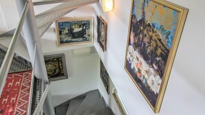 A staircase with a metal railing, a red patterned carpet, and several framed artworks on the walls.