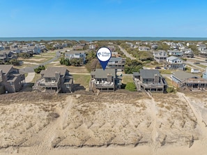 An aerial view of a coastal residential area with houses, sandy dunes, and a clear view of the ocean.