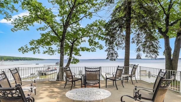 An outdoor seating area with a view of the lake, furnished with metal chairs and a white table. - Higgins Lake Lakefront Lodge with Private Sandy Beach - Sleeps 13 (Roscommon)