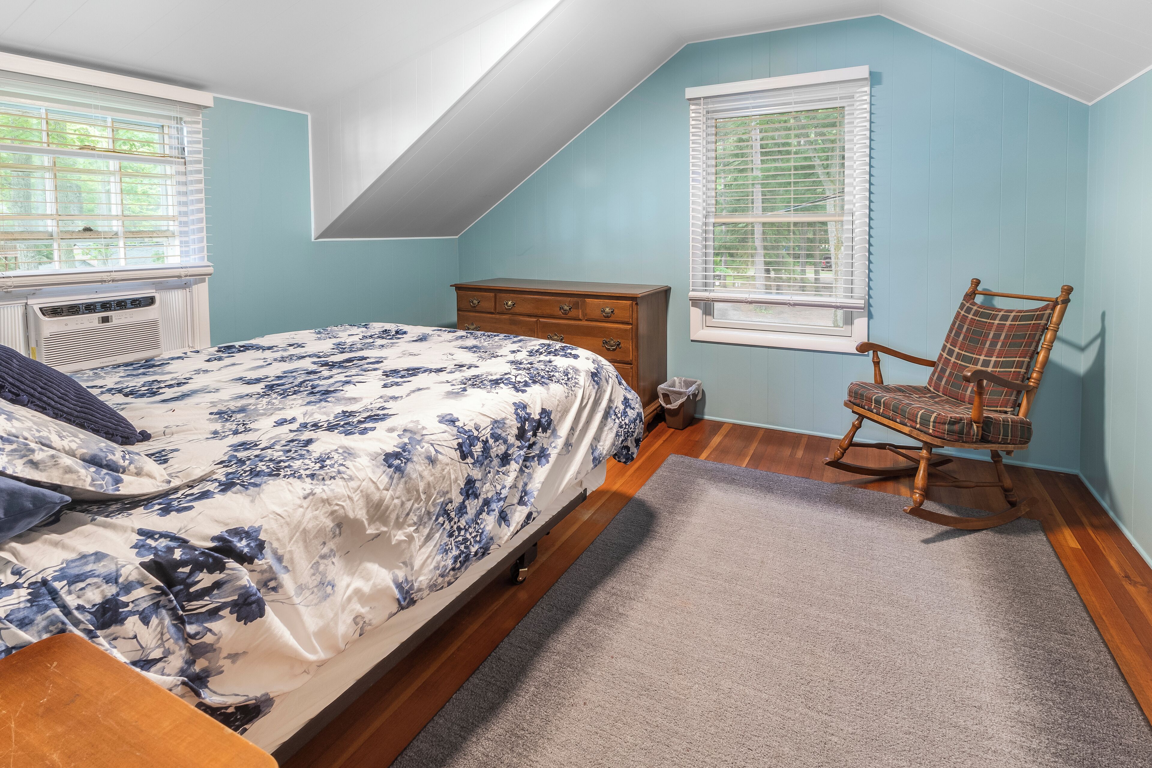 A bedroom with a bed, dresser, rocking chair, and two windows.
