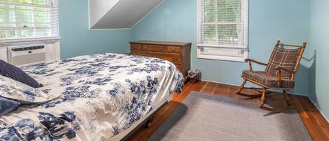 A bedroom with a bed, dresser, rocking chair, and two windows.