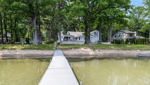 A wooden dock leading to a house with a large front porch, surrounded by trees and a body of water. - Higgins Lake Lakefront Lodge with Private Sandy Beach - Sleeps 13 (Roscommon)