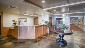 A hotel lobby with a reception desk, a large potted plant, and a carpeted hallway.