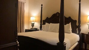 A four-poster bed with a wooden headboard, two bedside tables with lamps, and a curtain on the left side.