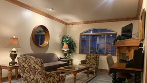 A living room with a sofa, two armchairs, a coffee table, a fireplace, a television, and a large mirror.