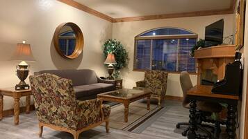 A living room with a sofa, two armchairs, a coffee table, a fireplace, a television, and a large mirror.