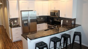 A modern kitchen with white cabinets, stainless steel appliances, a granite countertop, and four black bar stools. - Family-friendly Lakefront East Lake Okoboji Condo- Bridges Bay Resort (Arnolds Park)