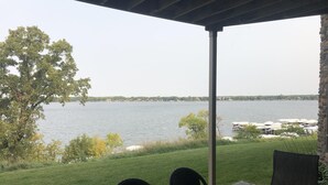 A covered patio with a view of a lake, a grassy lawn, and a dock with boats. - Family-friendly Lakefront East Lake Okoboji Condo- Bridges Bay Resort (Arnolds Park)