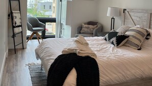 Ein modernes Schlafzimmer mit einem großen Bett, einem Flachbildfernseher, einem Schreibtisch mit Stuhl und Blick ins Freie.