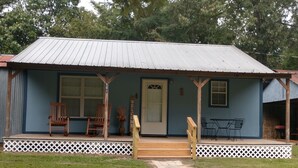 Une maison bleue avec un porche, une chaise en bois, une table et une porte ornée d’une pancarte indiquant « Bienvenue ».