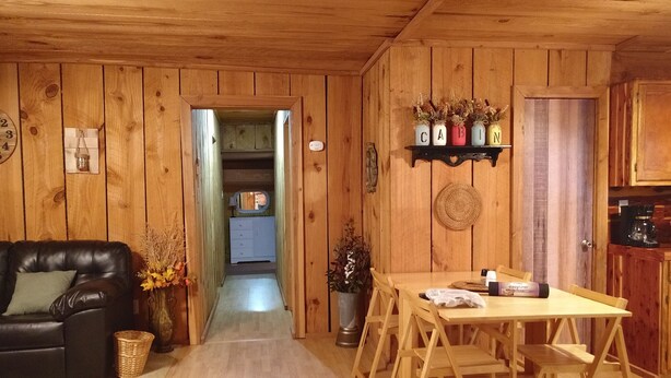 Un intérieur en bois comprenant un canapé, une table à manger avec des chaises, un coin cuisine et un couloir menant à une salle de bain.