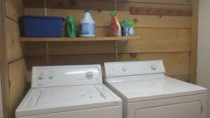 Un espace buanderie comprenant deux machines à laver blanches, un évier bleu et des étagères où sont rangés les produits de nettoyage.
