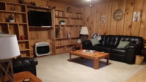 Un salon chaleureux avec un décor intérieur en bois, un canapé en cuir noir, une table basse en bois et un téléviseur fixé au mur.