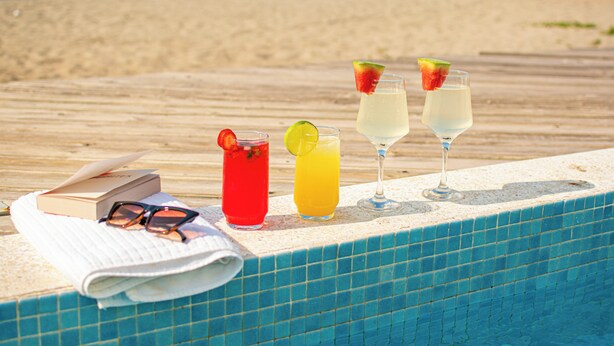 Un cadre agréable au bord de la piscine, avec des boissons, un livre et des lunettes de soleil, donnant sur une plage.