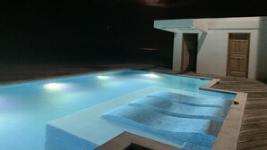 Une piscine avec une terrasse en bois et un petit bâtiment doté d’une porte.