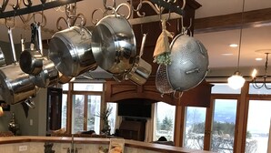 A kitchen with granite countertops, a gas stove, hanging pots, and a large window offering a view of a snowy landscape. - Gentleman’s Farm Mountain Views Gourmet Kitchen Fire Pit Hike Ski Sleep 10 Pets! (Oak Hill)