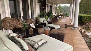 A covered outdoor seating area with wicker furniture, cushions, and potted plants. - Gentleman’s Farm Mountain Views Gourmet Kitchen Fire Pit Hike Ski Sleep 10 Pets! (Oak Hill)