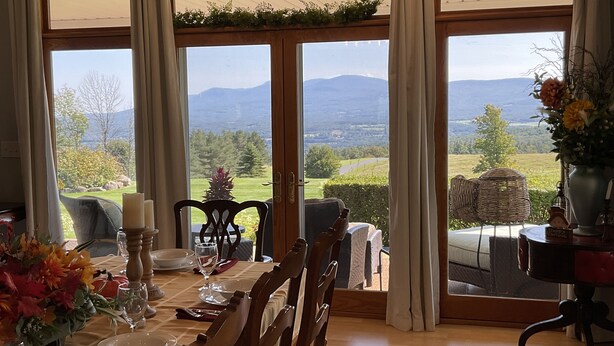 A dining area with a table set for four, large windows with curtains, and a view of a green landscape with mountains. - Gentleman’s Farm Mountain Views Gourmet Kitchen Fire Pit Hike Ski Sleep 10 Pets! (Oak Hill)