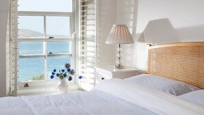 Una camera da letto con un letto, un comodino con una lampada, una finestra vista mare e un vaso con fiori.