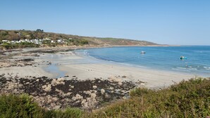 Una spiaggia costiera con zone rocciose, acqua blu cristallina e case sullo sfondo.