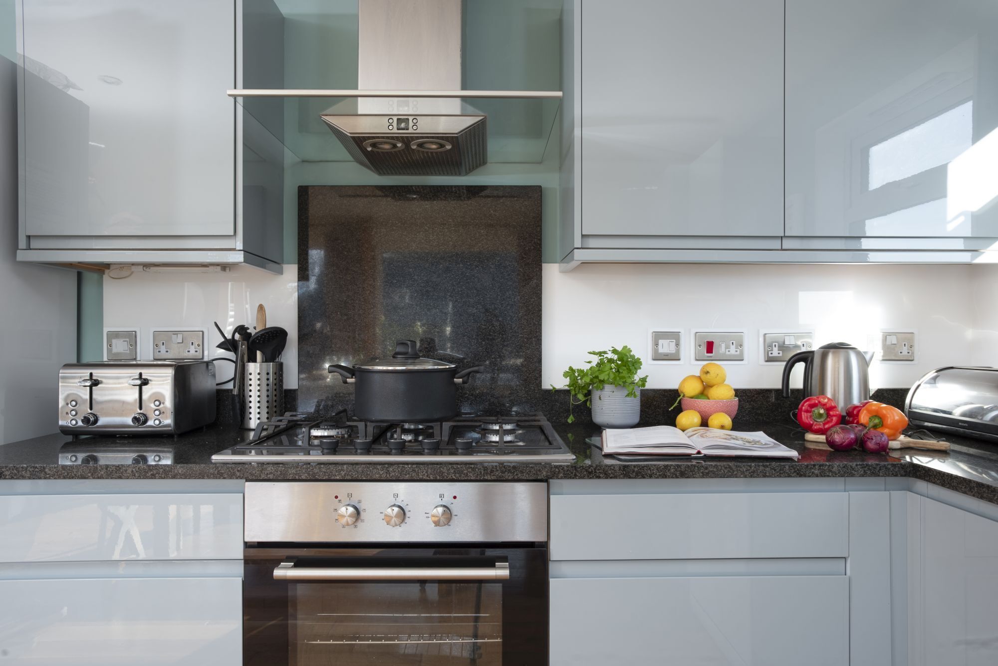 A modern kitchen with a gas stove, oven, and a toaster. There are vegetables and a book on the counter.