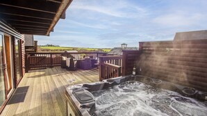 Un jacuzzi en una terraza de madera con asientos exteriores y vistas al campo.