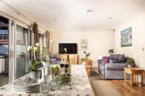 A modern living room with a dining area, a sofa, a TV, and a cityscape painting. - Lodge 40 - Resort & Spa/ Hot Tub/ Free Wi-Fi (St Columb Major)